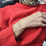 A close-up view of a person wearing a red sweater and a gold bracelet on their wrist.