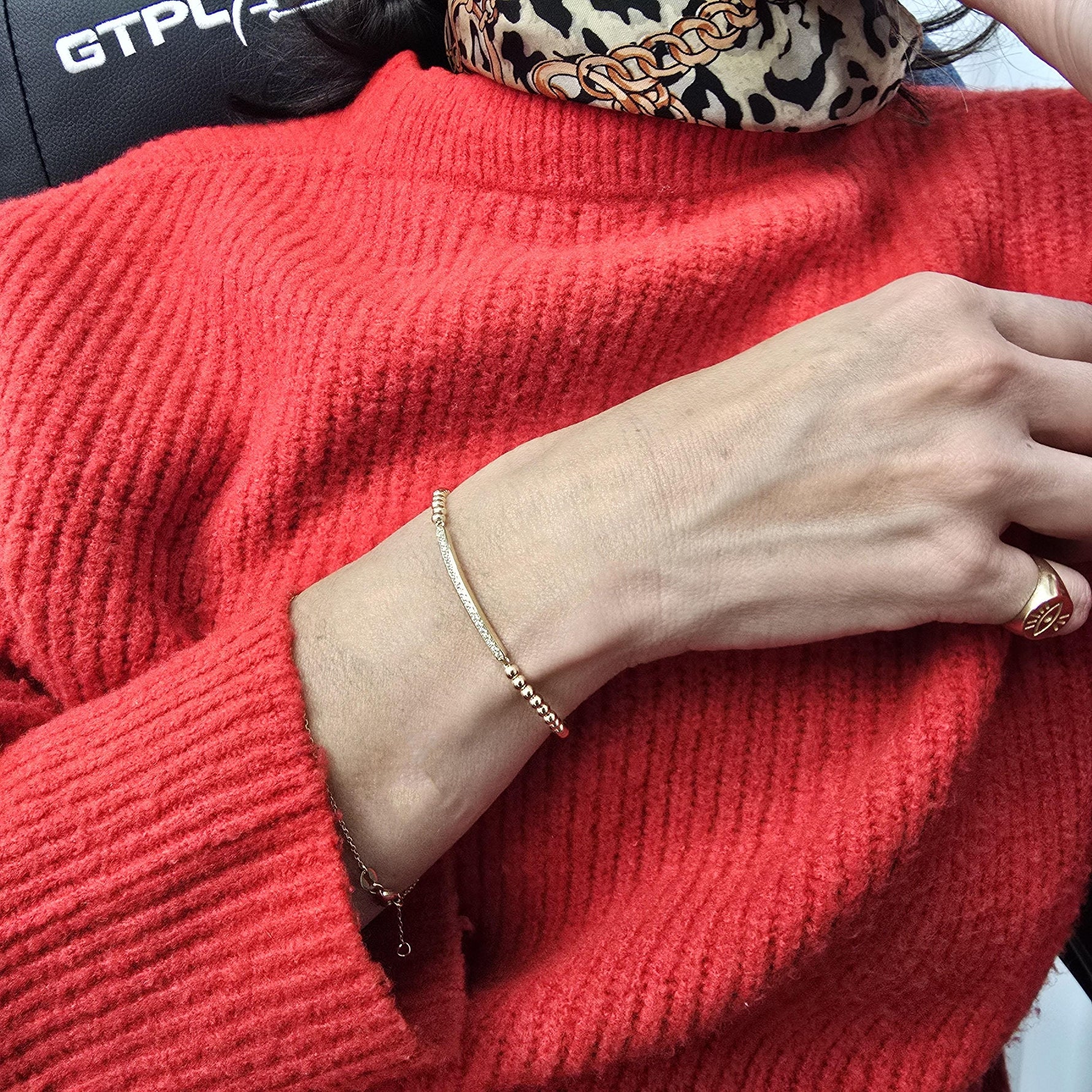 A close-up view of a person wearing a red sweater and a gold bracelet on their wrist.