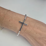 A silver cross-shaped bracelet is worn on a person&