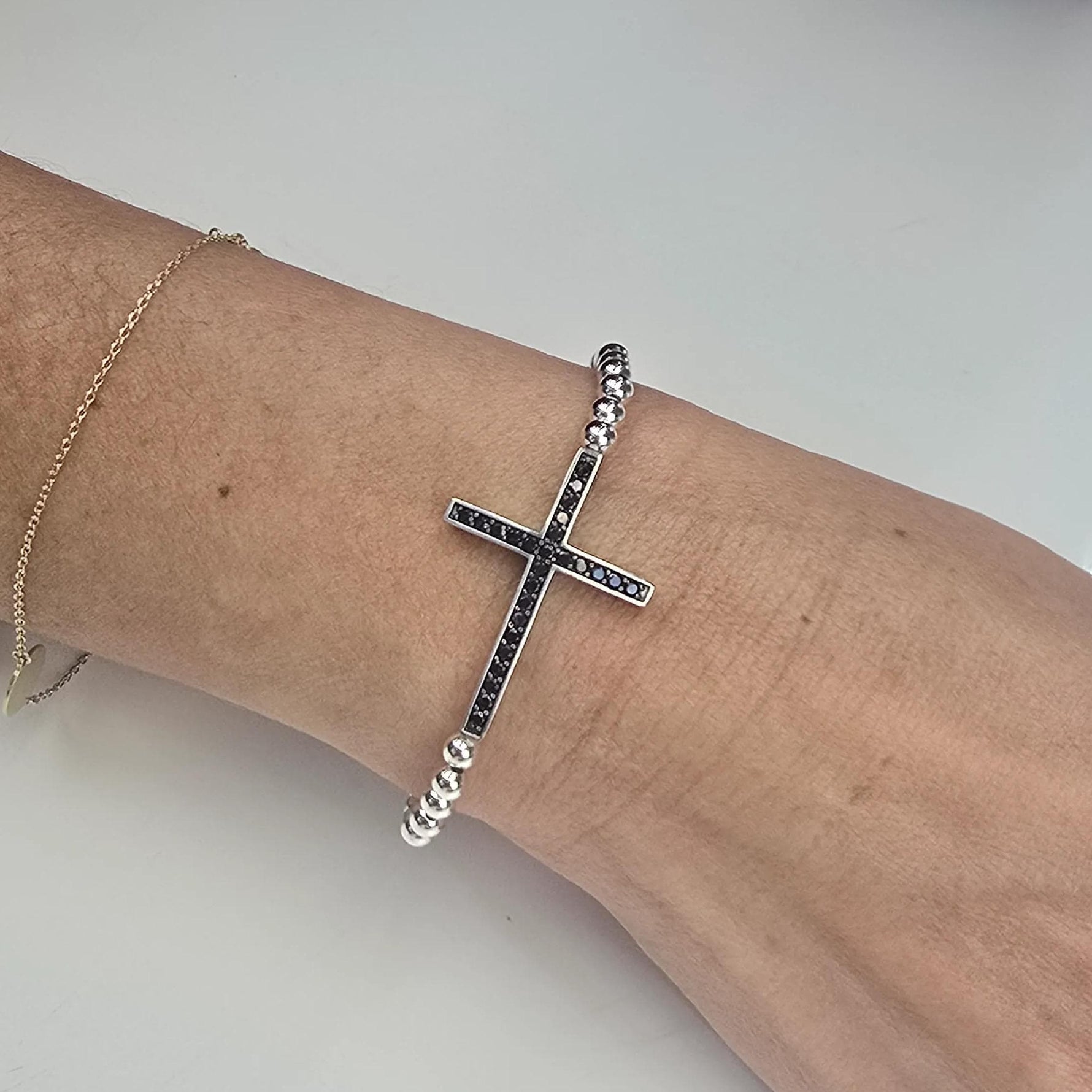 A silver cross-shaped bracelet is worn on a person&