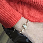 A gold-colored bracelet with a diamond-encrusted eye design is worn on a person&