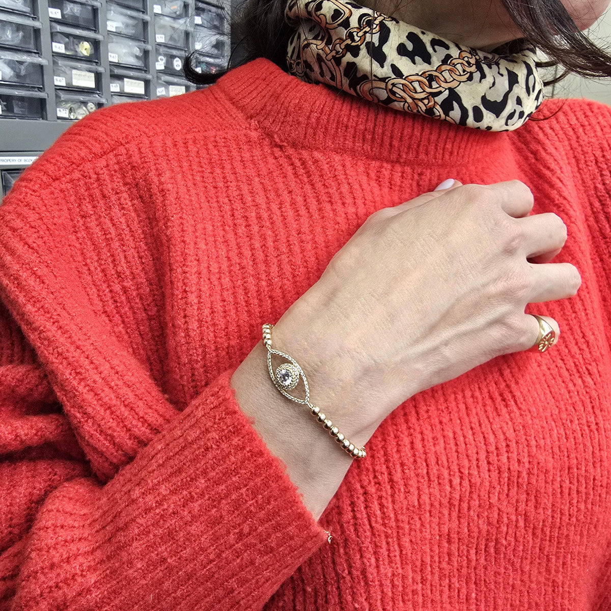 A person wearing a red sweater and a leopard print scarf is holding a bracelet with an eye design on their wrist.