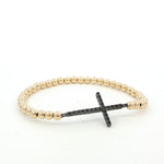 A gold-colored beaded bracelet with a black cross-shaped charm attached to it.