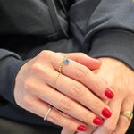 May include: Gold beaded ring with a blue evil eye charm. The ring is worn on a finger with red nail polish.