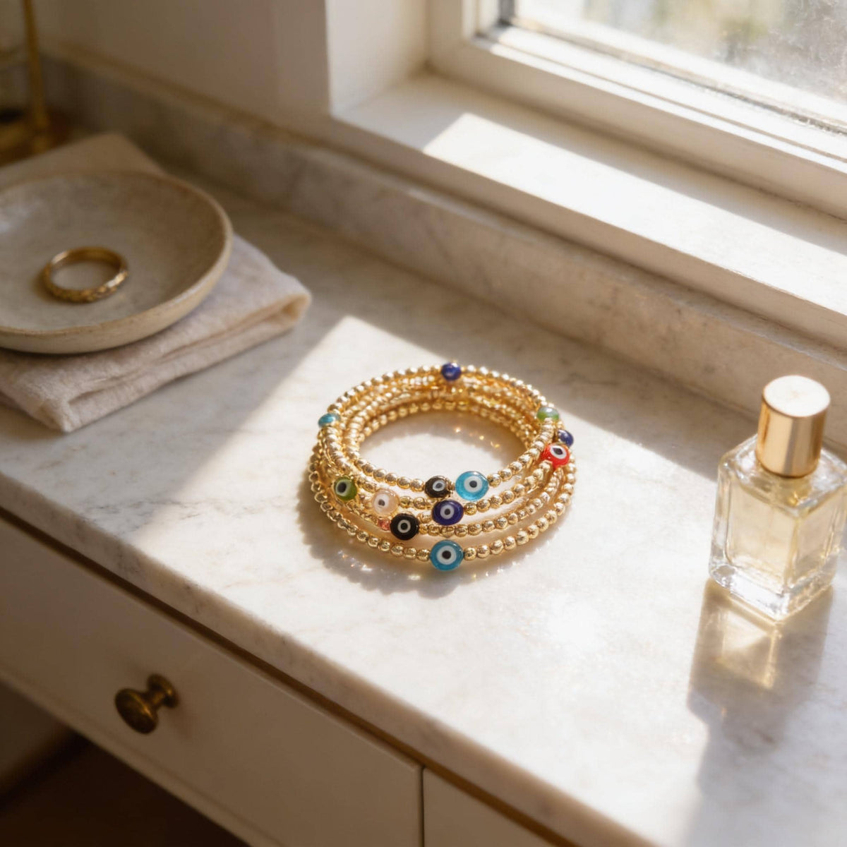 a marble countertop with a gold bracelet adorned with colorful beads, a ring, and a perfume bottle.