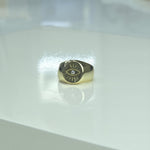 A gold ring with an eye design is placed on a white surface.