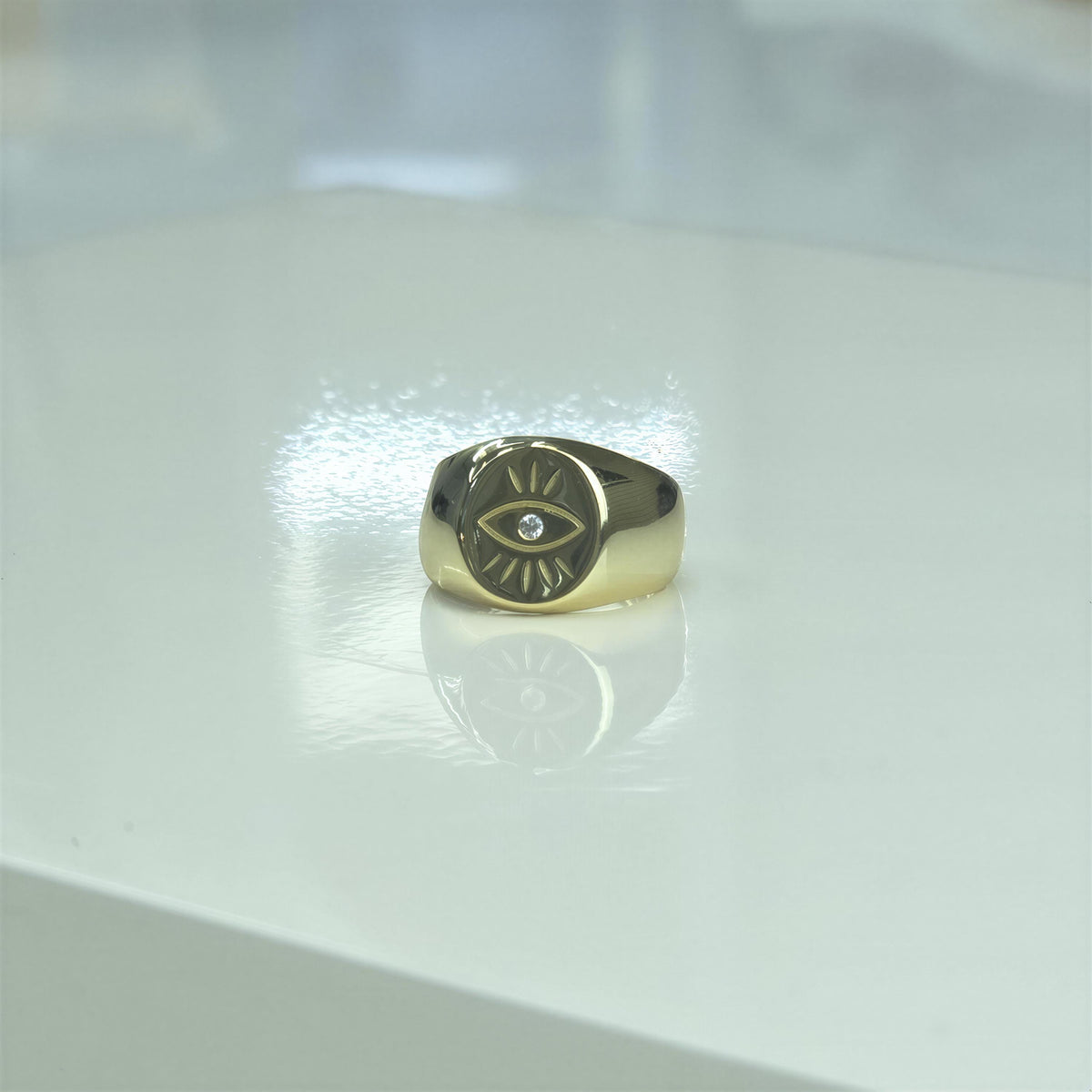 A gold ring with an eye design is placed on a white surface.
