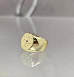 A gold ring with a large eye design on it, placed on a reflective surface.
