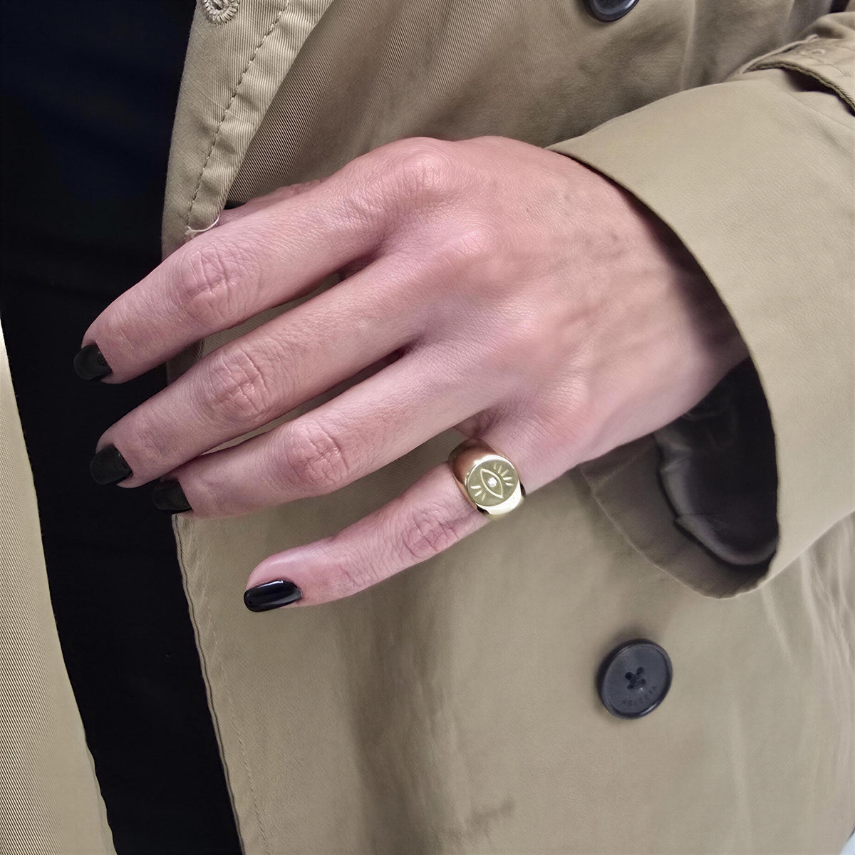 A close-up of a person's hand wearing a gold ring with a symbol on it, wearing a tan coat.