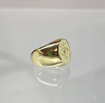 A gold ring with an eye design on it, placed on a reflective surface.