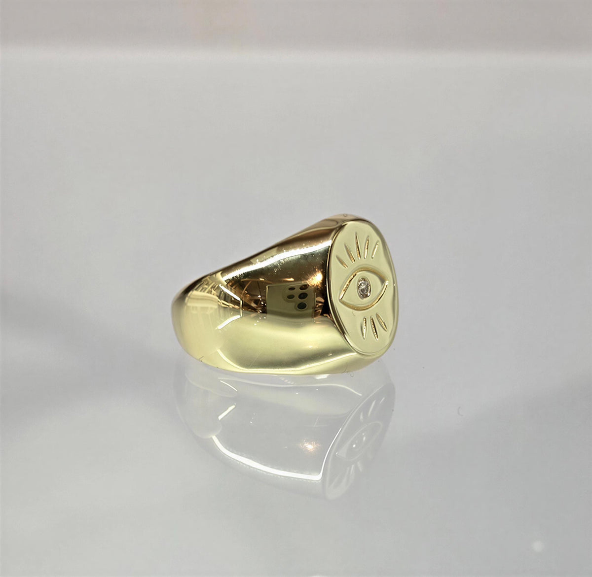 A gold ring with an eye design on it, placed on a reflective surface.