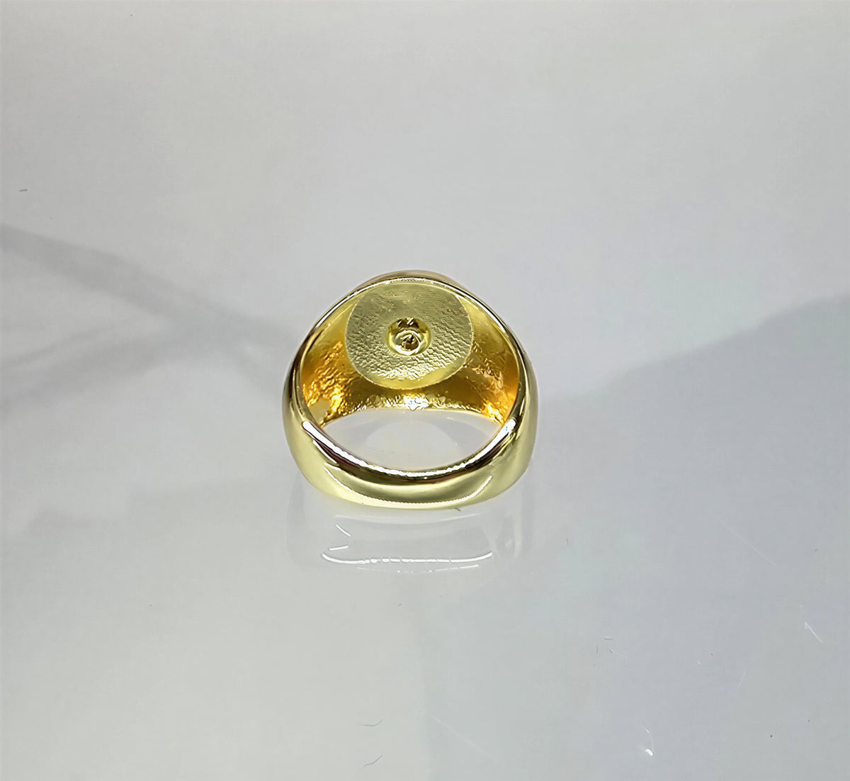 A gold ring with a small hole in the center, placed on a reflective surface.