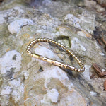 Isabella Celini gold-filled beaded stretch bracelet with a bamboo bar accent resting on a textured stone surface.