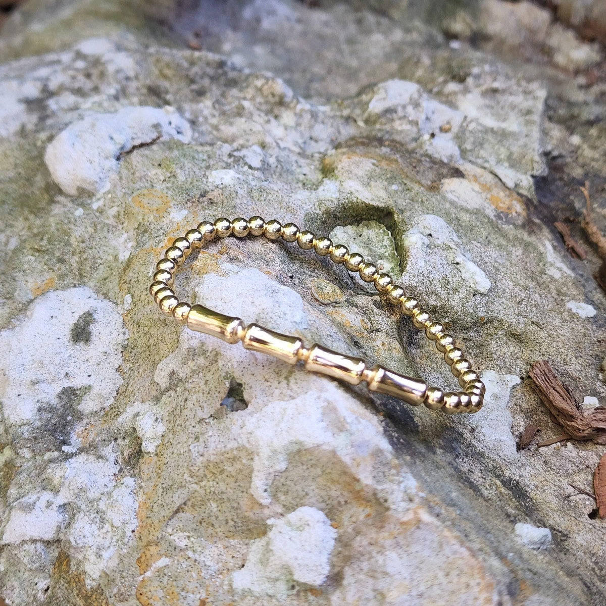 Isabella Celini gold-filled beaded stretch bracelet with a bamboo bar accent resting on a textured stone surface.